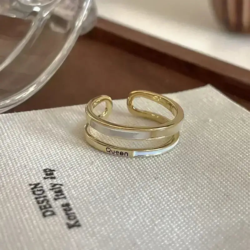 Gold-toned adjustable soul eater kid skull ring with two layered bands and a central white stripe engraved with queen
