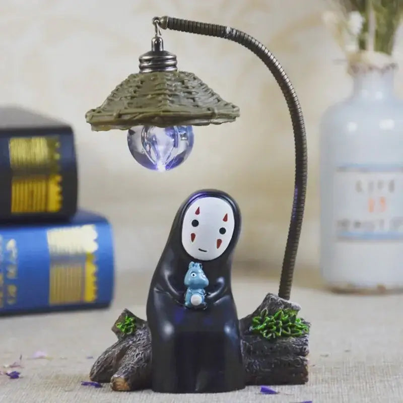 Black resin spirited away no face led desk lamp with olive green woven lampshade and flexible metal arm holding blue creature