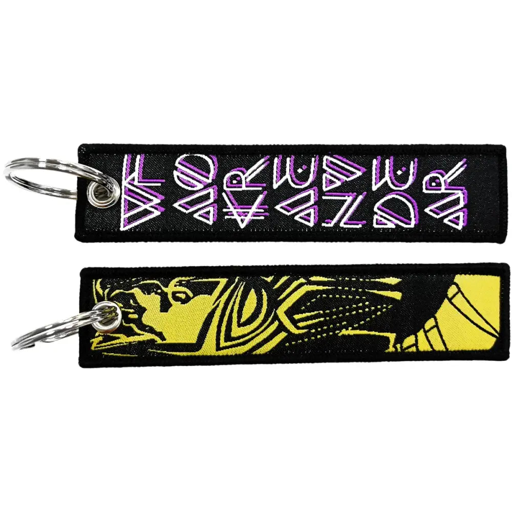 Two embroidered key fobs with purple geometric lettering and yellow stylized face on black fabric key tags with silver rings