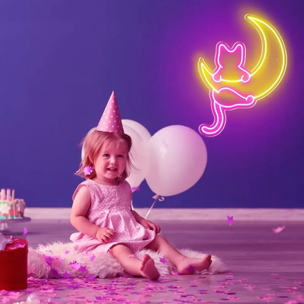 A young child in a pink dress sits near a colorful anime cat led neon sign birthday party neon wall decor