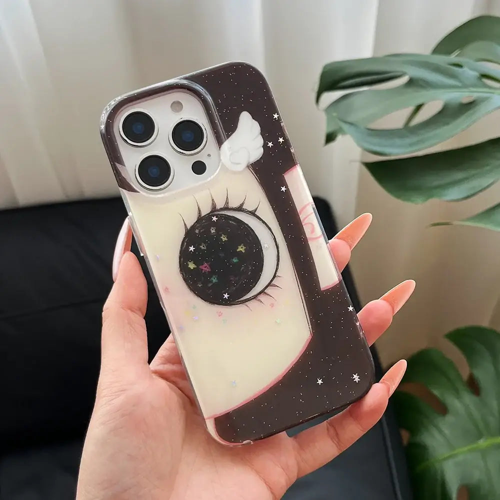 Black and cream phone case with whimsical crescent moon, long eyelashes, glittering stars, and a small white wing on back