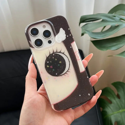 Black and cream phone case with whimsical crescent moon, long eyelashes, glittering stars, and a small white wing on back