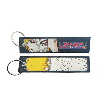 Two black embroidered anime lock keychains with bleach jet tags featuring red-eyed and yellow-haired characters