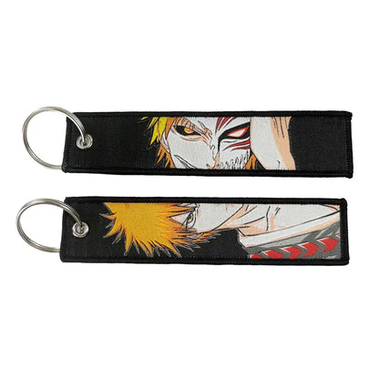 Black embroidered anime lock keychain featuring spiky yellow hair character and white mask on jet tag