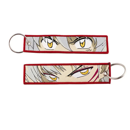 Red-bordered embroidered anime lock keychain with intense yellow eyes and silver hair jet tag design close-up