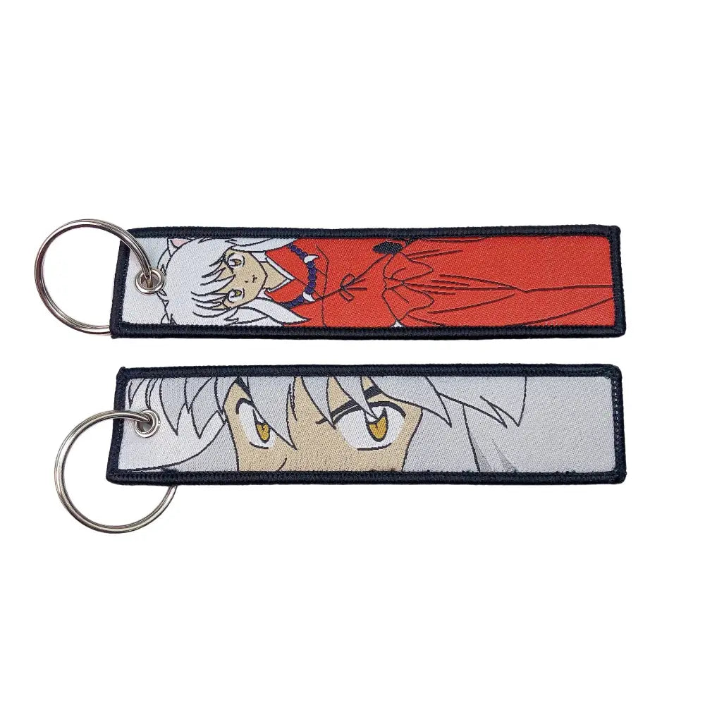 Two rectangular embroidered anime lock keychains featuring a white-haired figure in red and close-up eyes on silver background