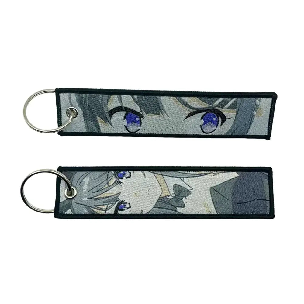 Two rectangular embroidered anime lock keychains with blue-eyed gray-haired character faces and black edges