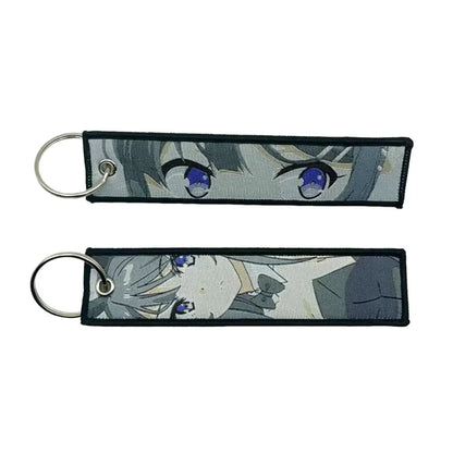 Two rectangular embroidered anime lock keychains with blue-eyed gray-haired character faces and black edges