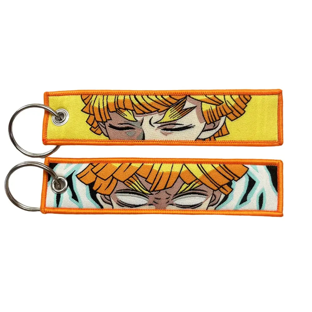 Two embroidered anime lock keychains with orange hair faces on yellow and black-and-white striped jet tags