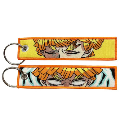 Two embroidered anime lock keychains with orange hair faces on yellow and black-and-white striped jet tags