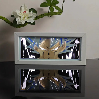 A glowing white-framed anime night light box featuring a blue and gold super saiyan goku paper-cutout for table decor