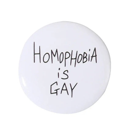 White circular anime pin brooch with durable tinplate and pin backing featuring black handwritten text homophobia is gay