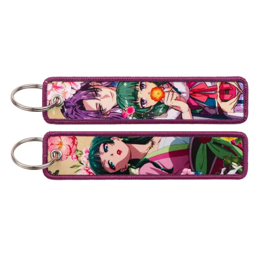 Two rectangular metal maomao key chains with purple stitched edges featuring anime characters in floral attire