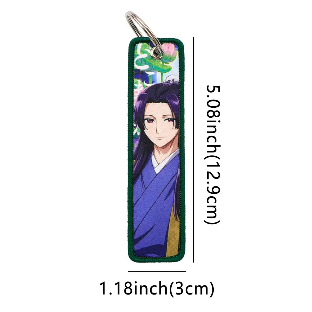 A metal rectangular maomao key chain with an embroidered anime character in a blue robe and green fabric edges
