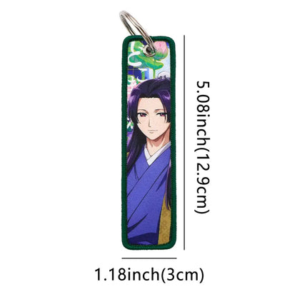 A metal rectangular maomao key chain with an embroidered anime character in a blue robe and green fabric edges