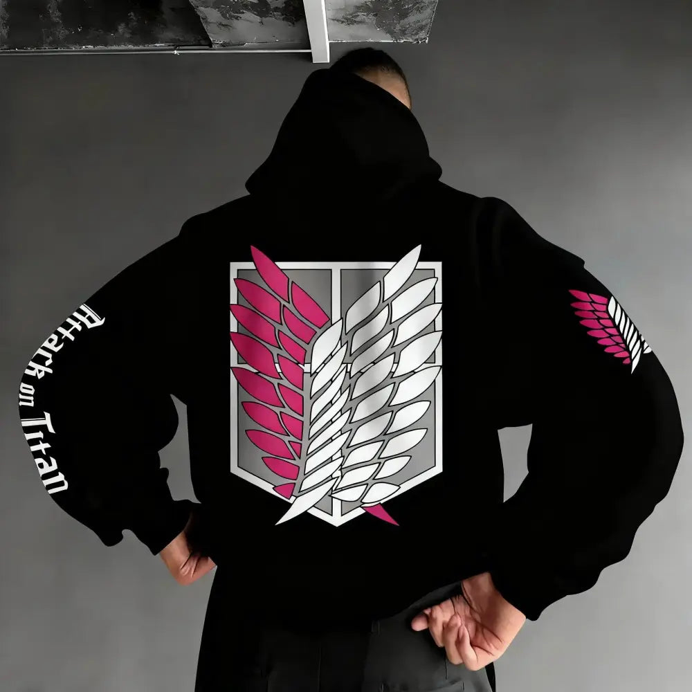 Back side of black oversized hoodie featuring pink and white winged emblem and attack on titan text on left sleeve
