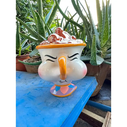 Whimsical white ceramic teacup jewelry box with orange handle and colorful base inspired by beast cogsworth clock