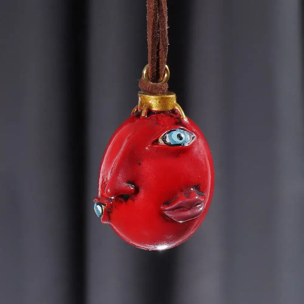 Glossy red resin pendant shaped like an egg with blue eyes and lips on brown leather cord berserk griffith behelit necklace