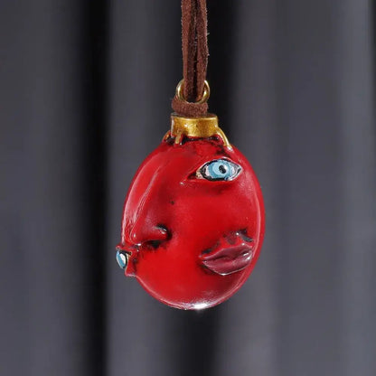 Glossy red resin pendant shaped like an egg with blue eyes and lips on brown leather cord berserk griffith behelit necklace