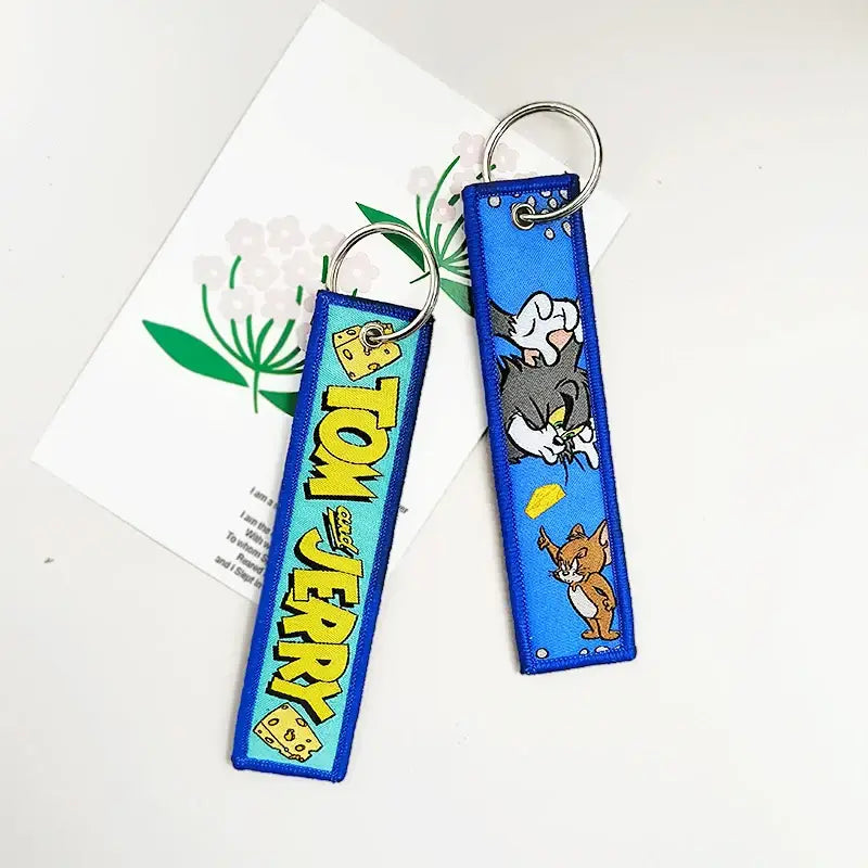 Blue embroidered tom and jerry keychain with yellow lettering paired with black clover asta leather key tag product