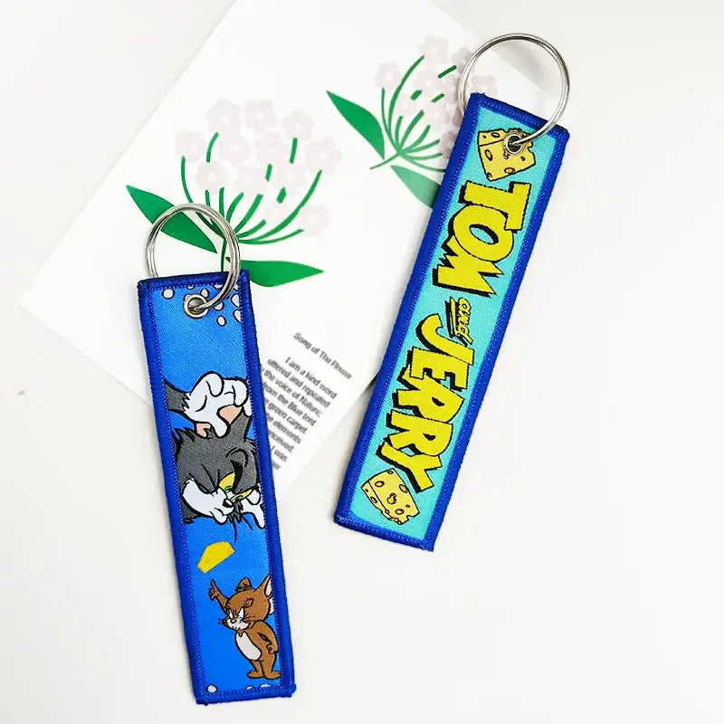 Blue embroidered tom and jerry keychain with yellow lettering and cheese motifs paired with black clover asta key tag leather design