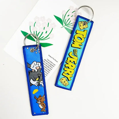 Blue embroidered tom and jerry keychain with yellow lettering and cheese motifs paired with black clover asta key tag leather design