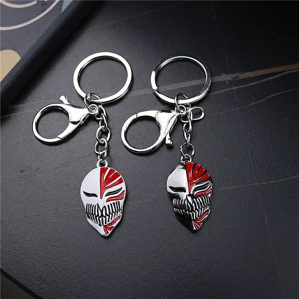 Two metal keychains with detailed half-red half-white ichigo hollow mask skull charms with black-lined eyes and teeth