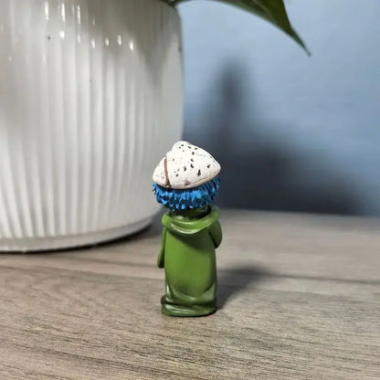 A small green neliel tu odelschwanck pvc figure with blue spiky hair and a white speckled hat measuring 6cm