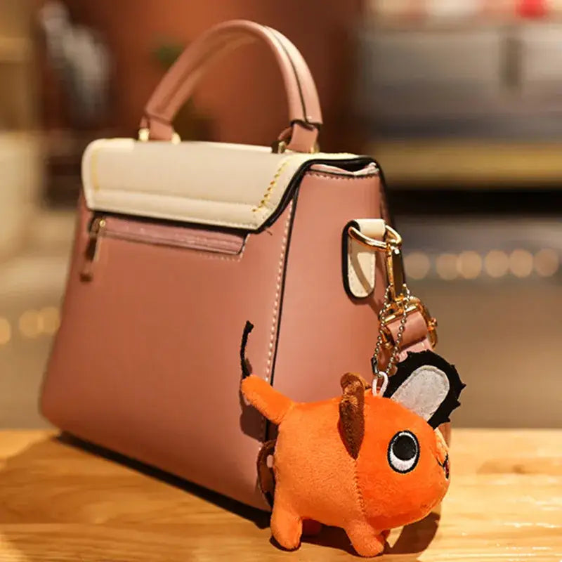 A pink and cream two-tone handbag with a soft stuffed orange chainsaw man plush pendant keychain attached