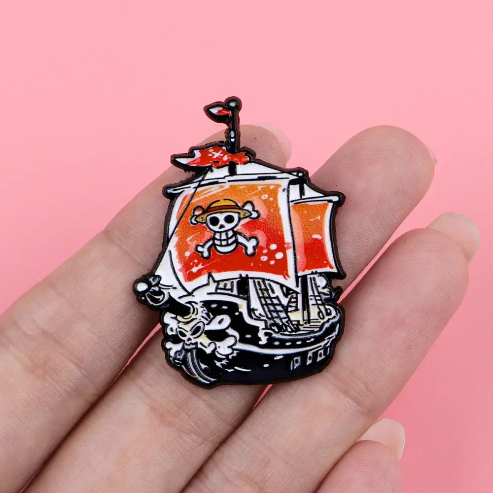 A vibrant orange and black pirate ship enamel pin with a skull flag and straw hat from a cute ship enamel pin set