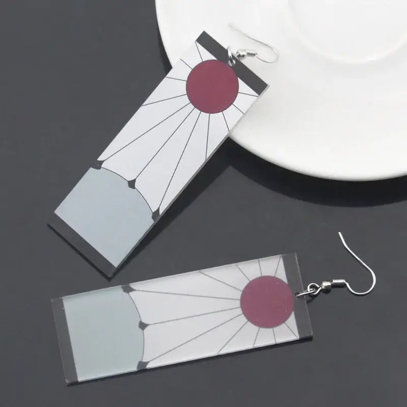 Rectangular acrylic demon slayer hanafuda earrings with maroon sun design and black radiating lines on white background