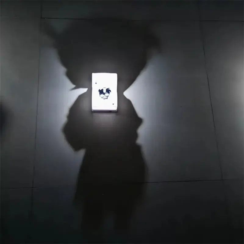 A glowing white led night light projector lamp featuring a black detective conan goku cartoon design on a dark tiled wall