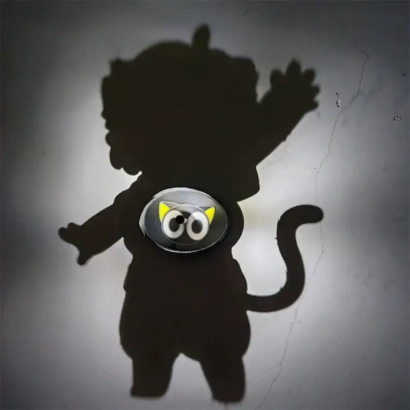 A shiny silver cat-shaped button with yellow ears and black eyes on the detective conan goku projector lamp night light