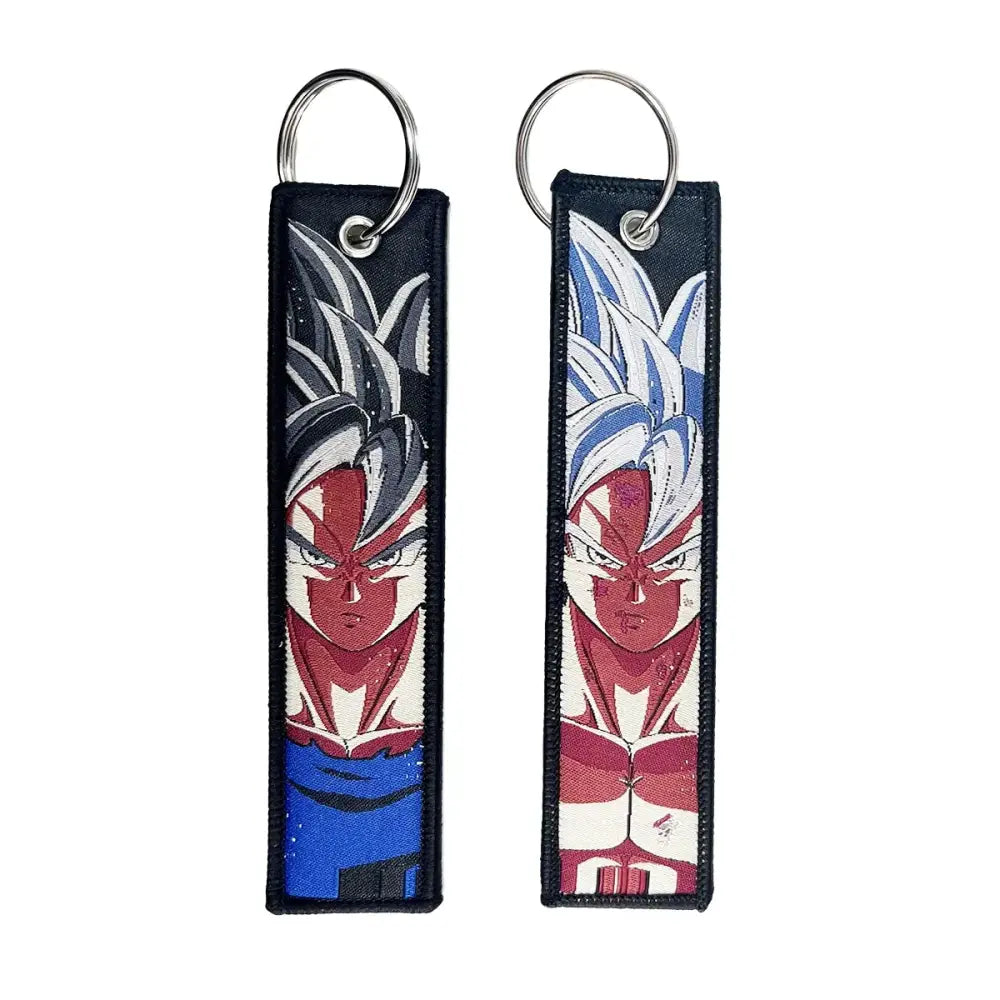 Two embroidered dragon ball goku keychain holders with spiky hair in black silver and blue white on dark fabric background