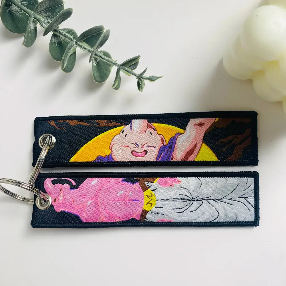 Two embroidered majin buu keychains with pink and purple design and silver details on dark fabric dragon ball keychain holder