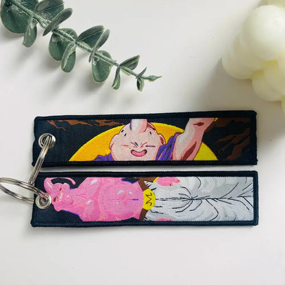 Two embroidered majin buu keychains with pink and purple design and silver details on dark fabric dragon ball keychain holder