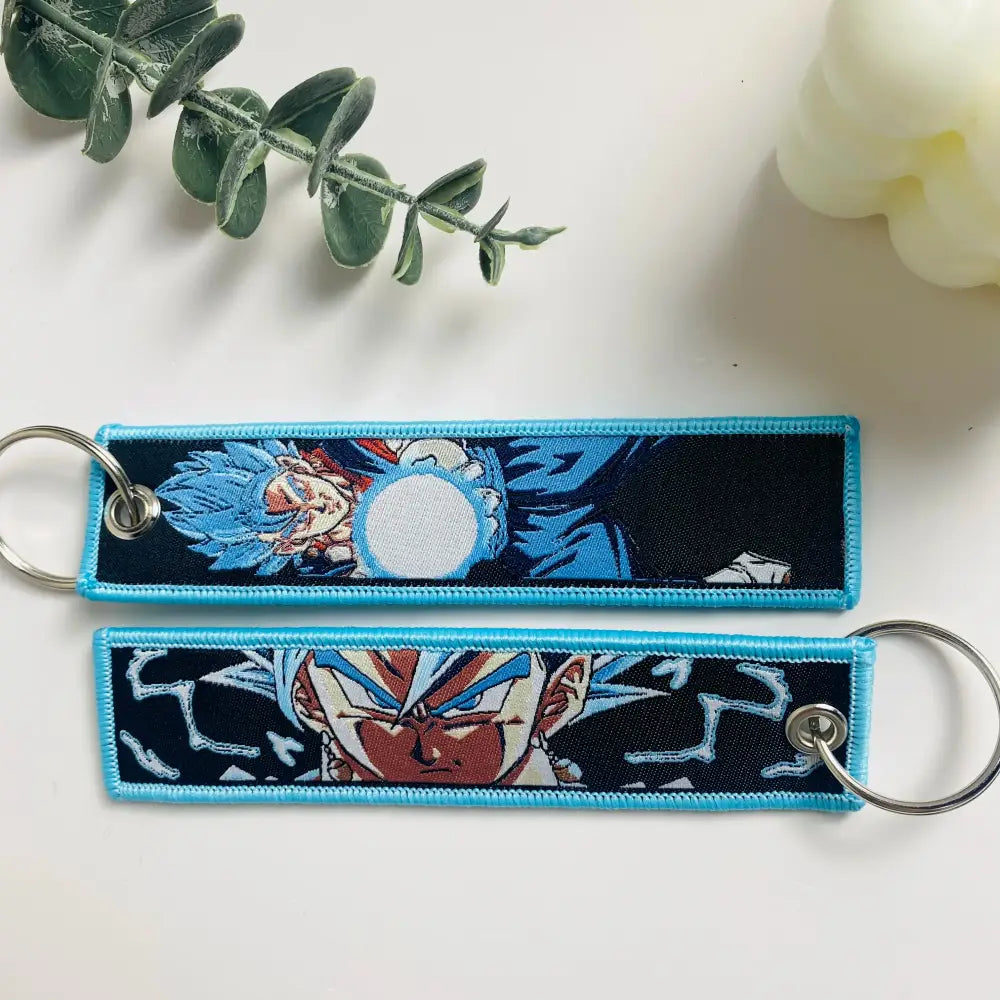 Two embroidered dragon ball goku keychain holders with blue and black fabric and silver metal rings