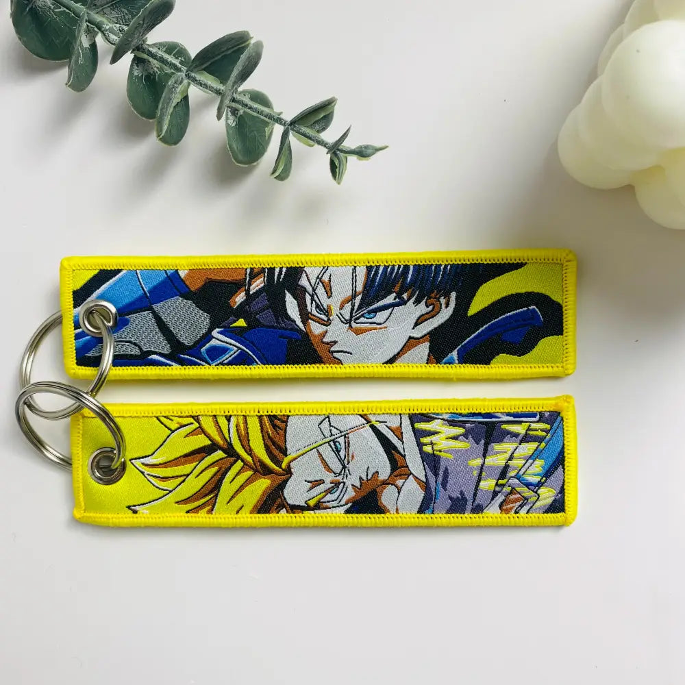 Two yellow-bordered embroidered dragon ball goku keychain holders featuring anime characters in blue black and gold hair design