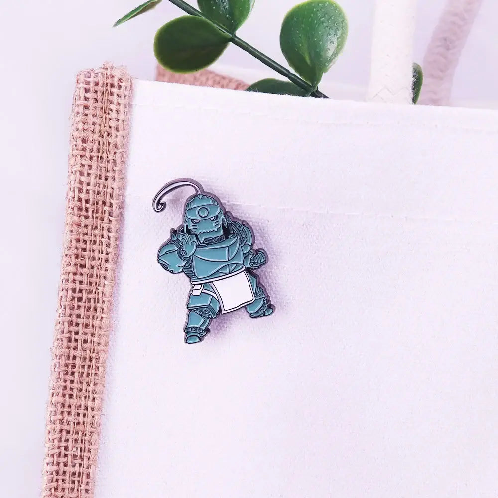 Teal enamel alphonse elric pin badge featuring a stylized armored character with a white apron and curved metal clasp