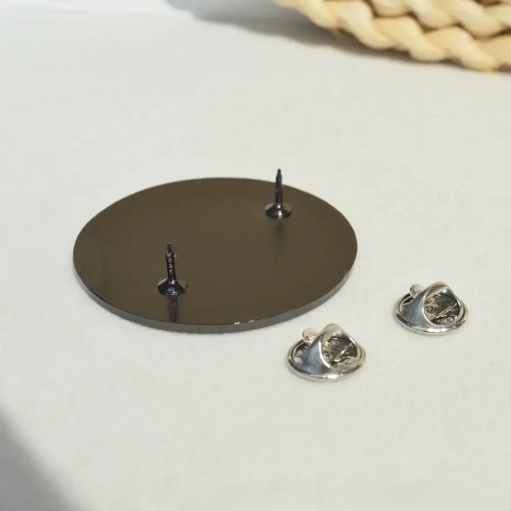 Back side of a sleek dark gray metal badge pin backing with two silver fasteners for fullmetal alchemist edward elric