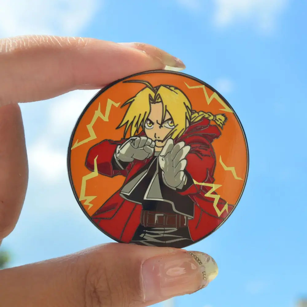 A circular metal badge enamel pin featuring fullmetal alchemist edward with blonde hair and a red coat on orange background