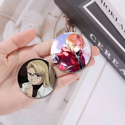 Two circular fullmetal alchemist enamel brooches featuring a blonde figure in glasses and an orange-haired figure with roses