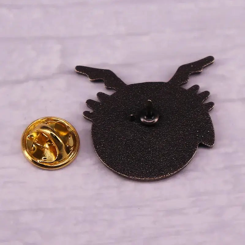 Black fullmetal alchemist enamel pin with stylized winged creature design and gold-toned metal badge clasp