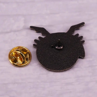 Black fullmetal alchemist enamel pin with stylized winged creature design and gold-toned metal badge clasp