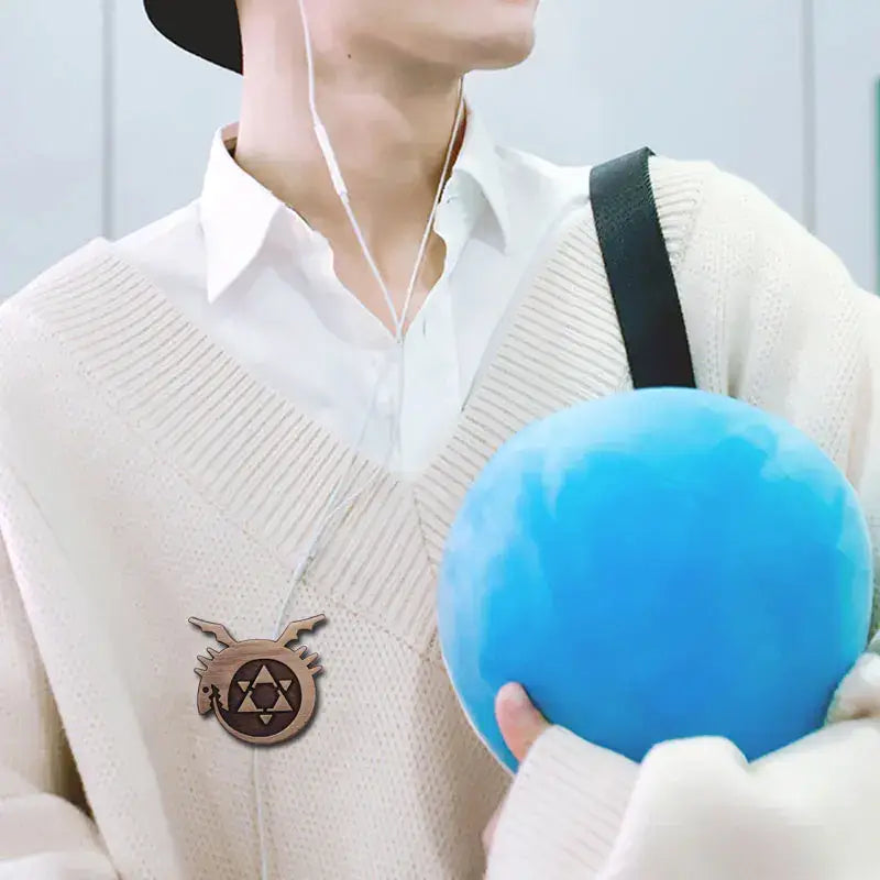 Blue spherical stress ball held in hand alongside fullmetal alchemist logo enamel pin metal badge collectible