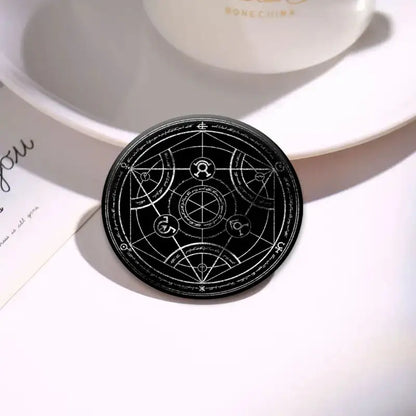 Black circular enamel pin featuring intricate white geometric and mystical symbols from fullmetal alchemist roy mustang