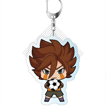 Chibi soccer player keychain with brown spiky hair holding black and white football in orange and black jersey and green shorts acrylic pendant from game inazuma eleven 11