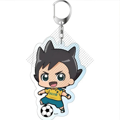 A clear acrylic keychain featuring a chibi boy in yellow island jersey and teal shorts kicking a soccer ball from game inazuma eleven