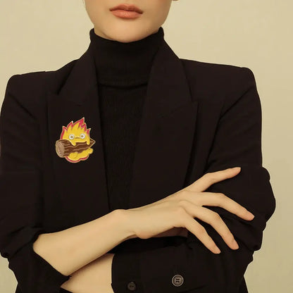 A charming yellow and red flame-themed moving castle calcifer enamel pin featuring a cute cartoonish log with googly eyes