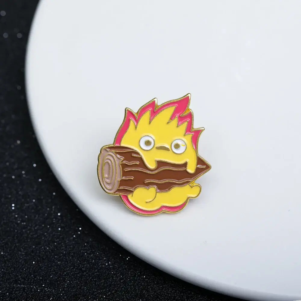 Howls moving castle calcifer enamel pin features a yellow flame character with pink tips on a brown log brooch